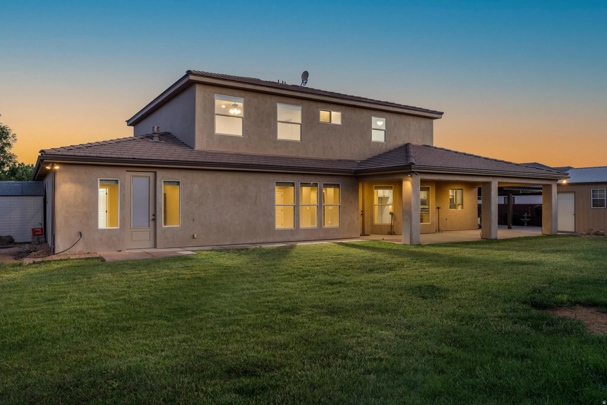 Rear exterior featuring a covered patio, multiple windows, and a manicured lawn