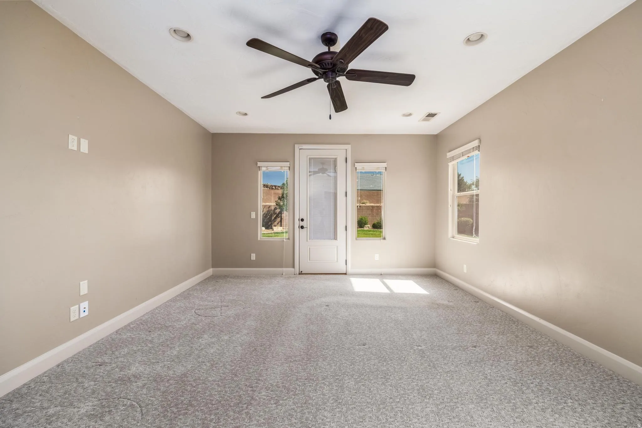 Spacious room featuring neutral wall paint, gray carpet flooring, a ceiling fan, recessed lighting, and a glass-paneled door with side windows
