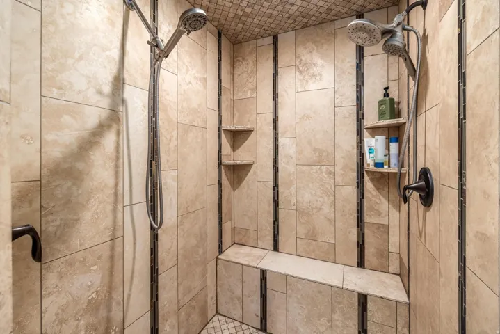 Tiled shower enclosure featuring a built-in bench, dual shower heads, and integrated corner shelving