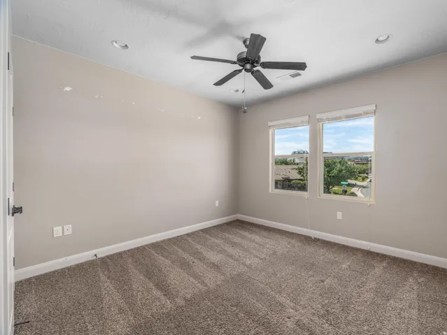 Neutral-toned room featuring a ceiling fan with integrated lighting, recessed ceiling lights, and two windows providing outdoor illumination