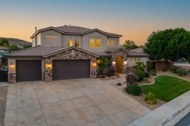 Stucco and stone facade property featuring a tile roof, multi-car garage, concrete driveway, and established landscaping