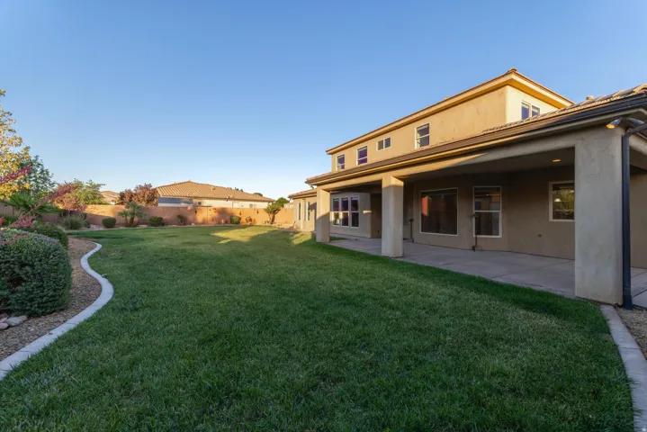 Expansive green lawn with a curved concrete border, mature landscaping, and a covered patio area