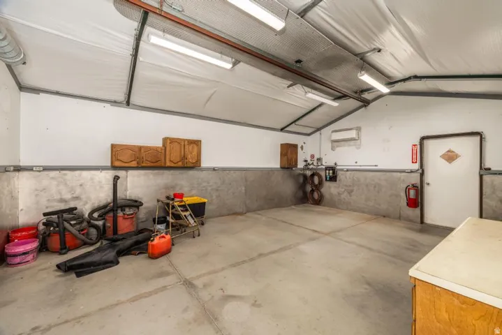 Spacious utility area featuring a concrete floor, high ceilings, fluorescent lighting, a white entry door, and wall-mounted cabinetry