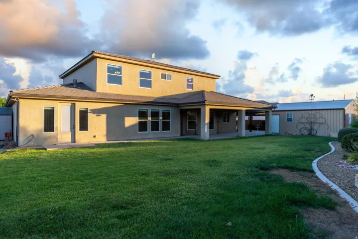 Expansive grassy backyard featuring a covered patio, stucco exterior, multiple windows, and a detached outbuilding