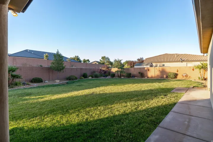 Expansive backyard featuring a lush green lawn, full perimeter block wall, mature landscaping, and an extended concrete patio