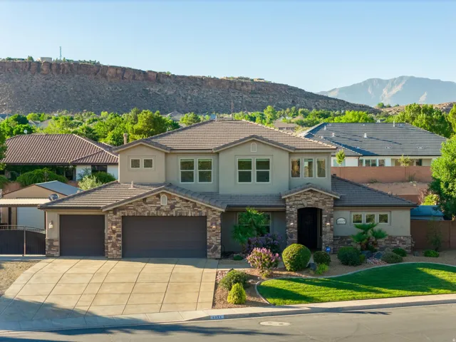 Two-story residence featuring a stone and stucco exterior, a tile roof, a multi-car garage, mature landscaping, and mountain scenery