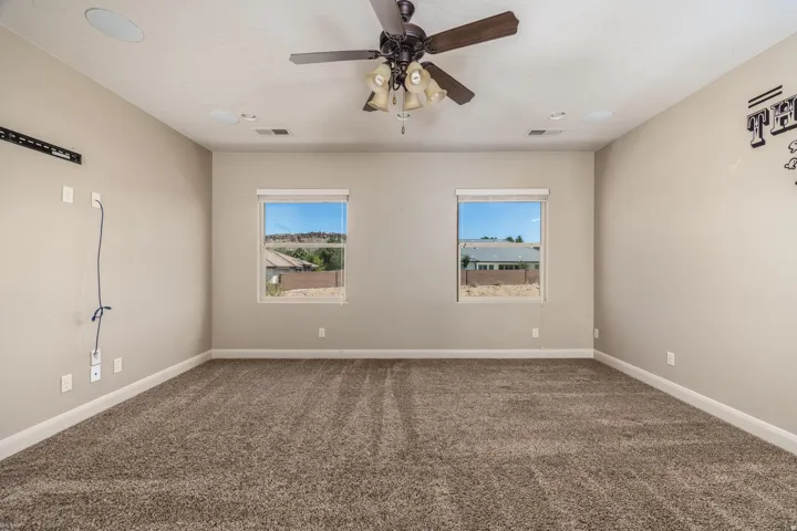 Carpeted room featuring two windows, a ceiling fan with integrated lighting, and recessed ceiling speakers