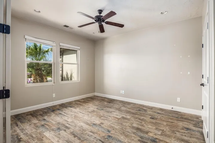 Room featuring wood-finish flooring, two windows with roller shades, a ceiling fan with integrated lighting, and recessed ceiling lights