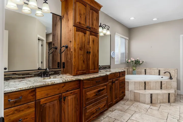 Spacious bathroom featuring dual wood vanities with granite countertops, integrated sinks, and individual mirrors