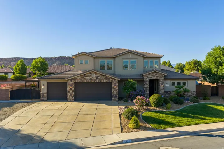 Two-story stucco residence featuring stone accents, a multi-car driveway, and an arched entry with a decorative metal gate