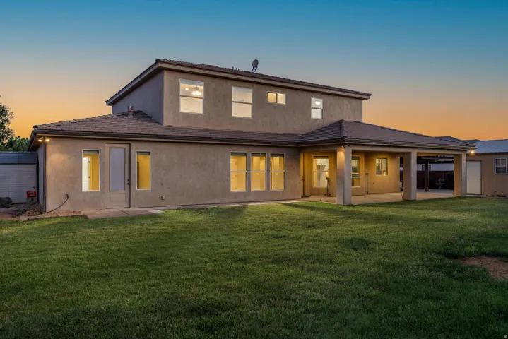 Rear exterior featuring a covered patio, multiple windows, and a manicured lawn