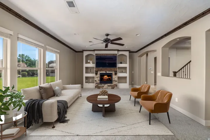 Spacious living area featuring a stone fireplace with a wood mantel, built-in shelving, and large windows