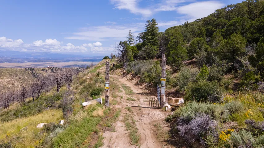 Gated dirt road offering access to a mountainous property with abundant natural foliage and distant valley scenery