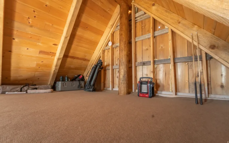 Attic space featuring pitched knotty pine wood paneling, exposed wood beams, a prominent natural wood post, and wall framing