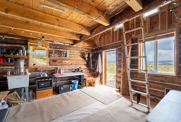 Rustic interior featuring exposed log walls, a wood plank ceiling with exposed beams, and a large window