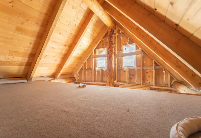 Spacious attic space featuring wood-paneled walls, exposed wood beams, and two dormer windows