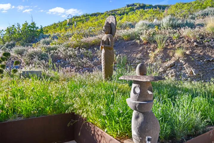 Landscaped hillside featuring natural vegetation, stone sculptures, and a clear blue sky
