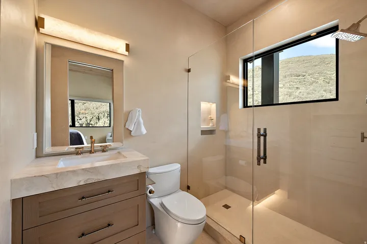Spacious bathroom featuring a frameless glass shower enclosure with a rainfall showerhead, a built-in shower niche with accent lighting, and a linear window