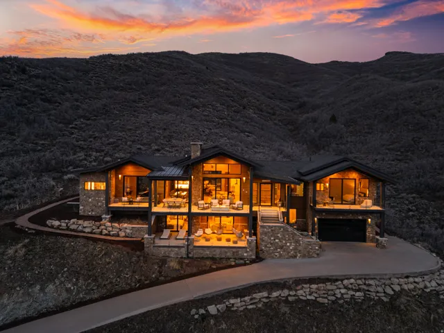 Contemporary mountain-style residence featuring extensive stone veneer, dark wood siding, multiple expansive balconies, a two-car garage, and a concrete driveway