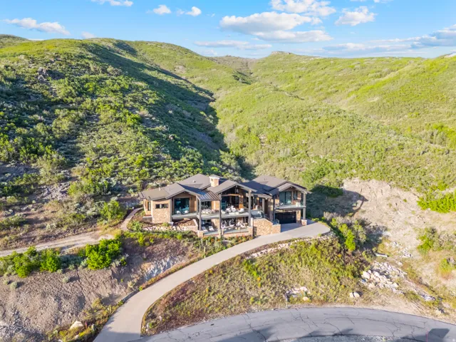 Hillside residence featuring stone and wood-clad exterior, multiple levels of balconies, a paved driveway, a multi-car garage, and a sloped terrain backdrop