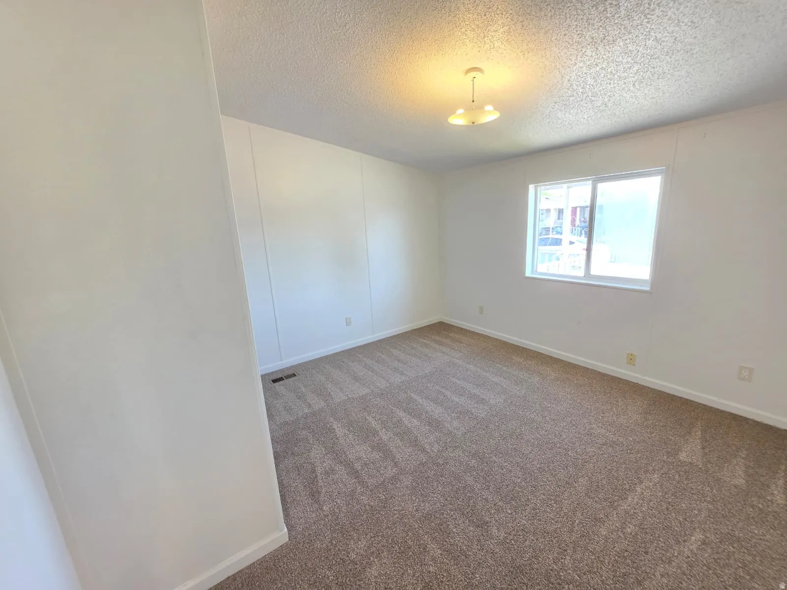 Carpeted room featuring a white ceiling and walls, a window with a white frame, baseboard trim, and a ceiling light fixture