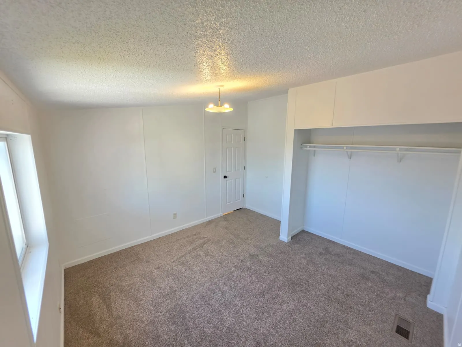 Bright room featuring neutral-toned carpet, white paneled walls, and a recessed clothing rod and shelf