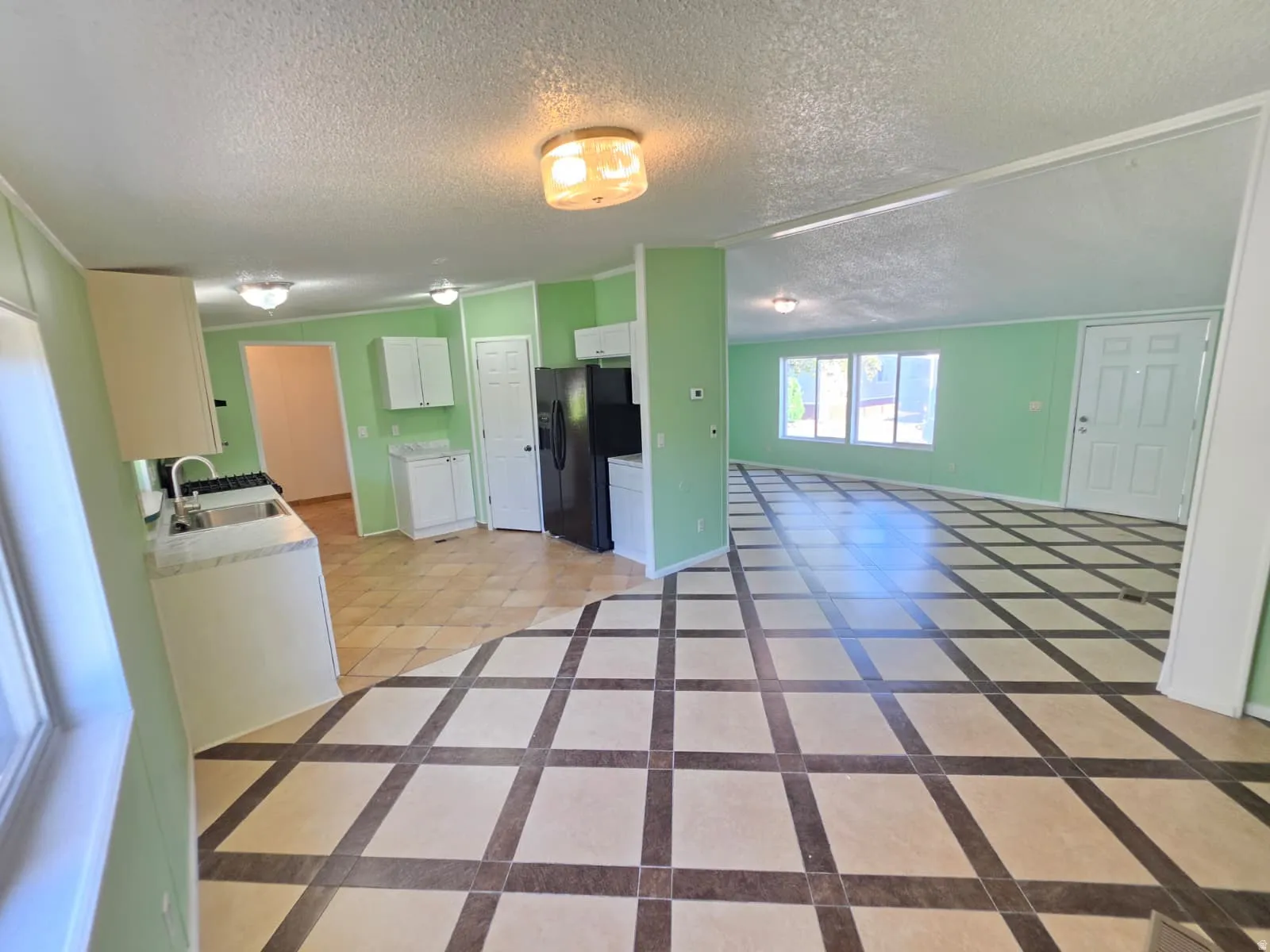 Open-concept living space featuring patterned tile flooring, light green walls, multiple windows, and a front entry door with vertical panels