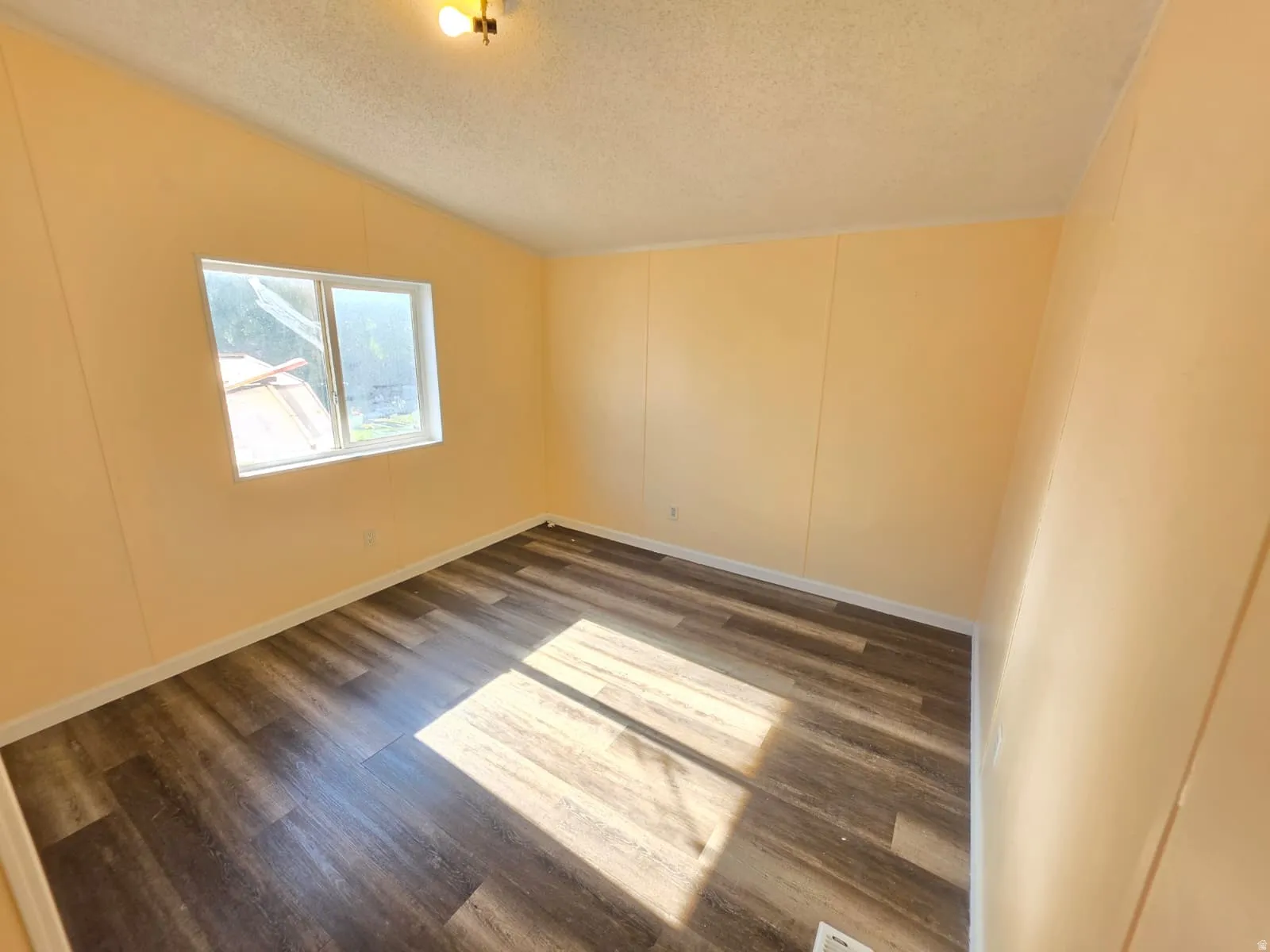 Room with wood-finish flooring, a window, and a ceiling-mounted light fixture