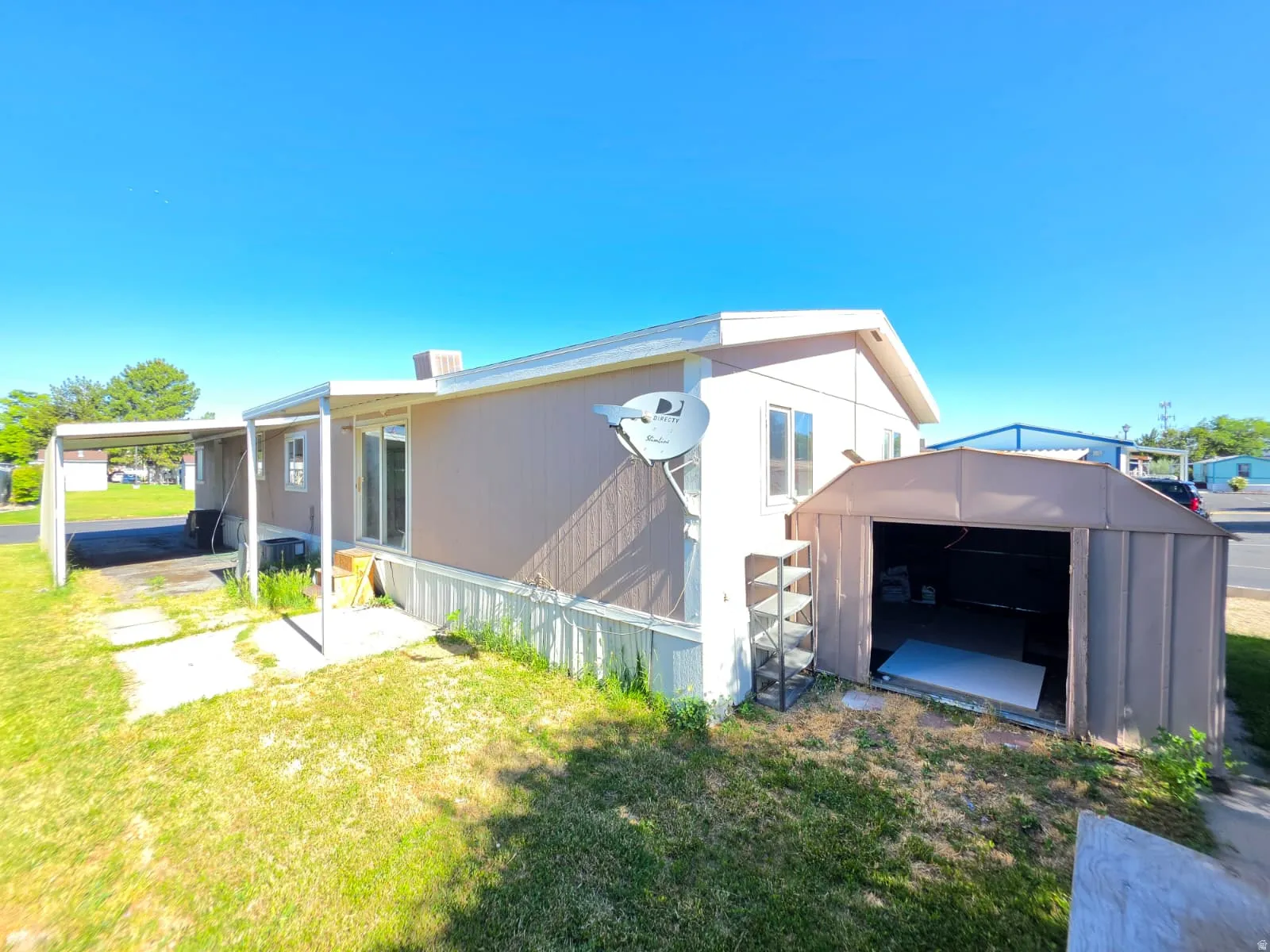 Exterior residence with tan siding, a covered patio, and a separate storage shed