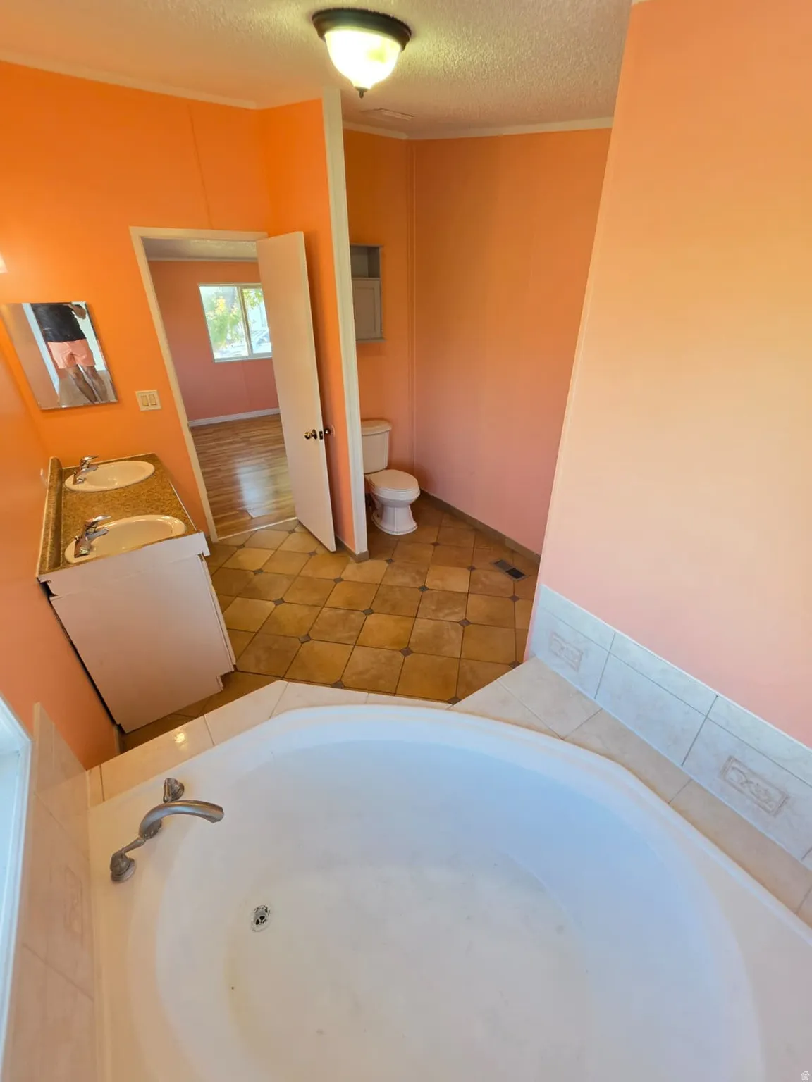 Bathroom featuring a corner soaking tub with tile surround, double vanity with two undermount sinks and a granite-style countertop, and patterned tile flooring