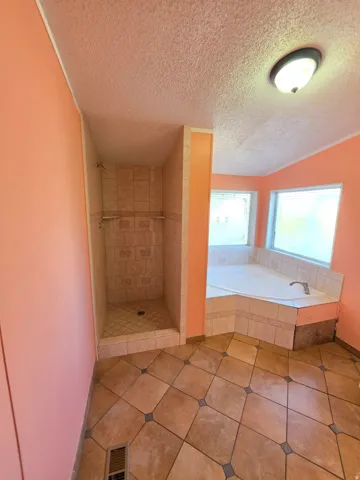 Bathroom featuring a corner soaking tub, a tiled shower enclosure, ceramic tile flooring, and a flush-mount ceiling light fixture