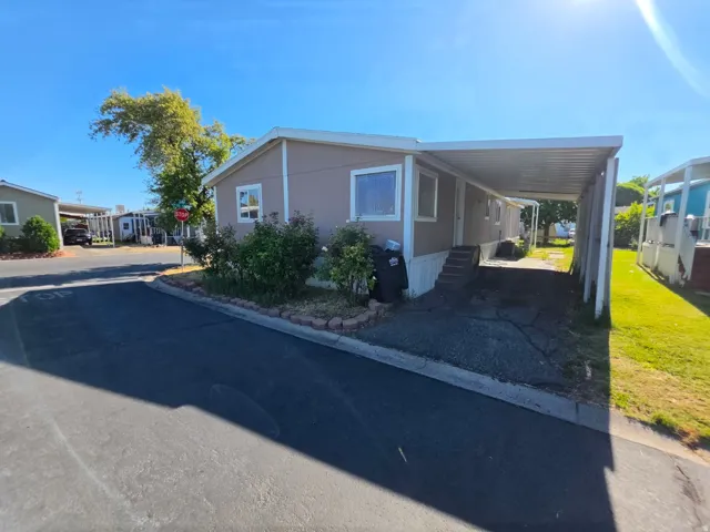 Single-story residence featuring a neutral-toned exterior, white window trim, a covered carport, a paved driveway, and established front landscaping