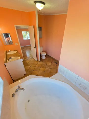 Bathroom featuring a corner soaking tub with tile surround, double vanity with two undermount sinks and a granite-style countertop, and patterned tile flooring