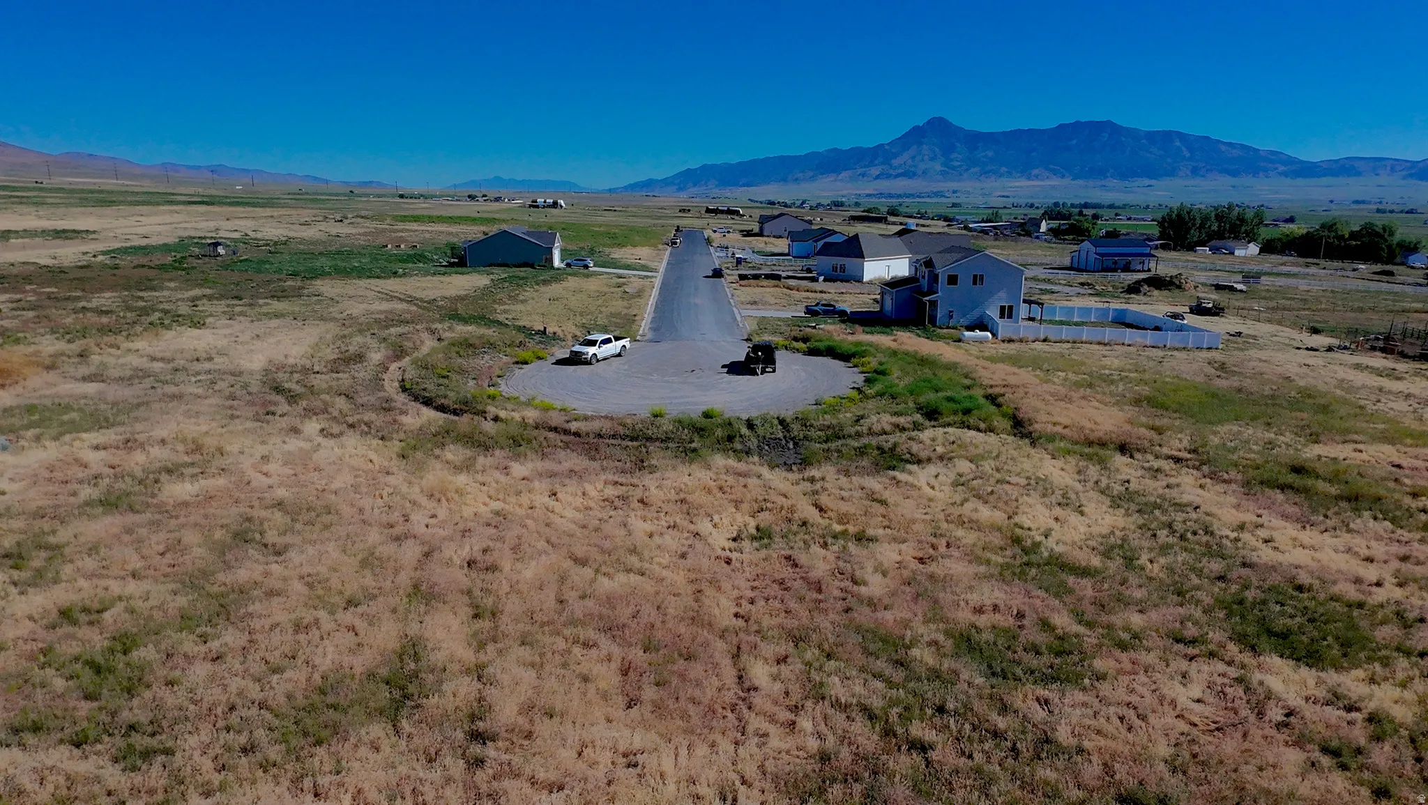 Expansive undeveloped lot presenting clear land, a paved road, and distant mountain scenery