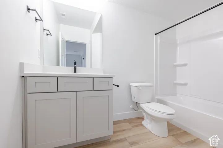 Bathroom featuring a light gray vanity with a solid surface countertop, matte black faucet, wall-mounted mirror, wood-finish flooring, and a white acrylic tub and shower combination with a matte black shower rod