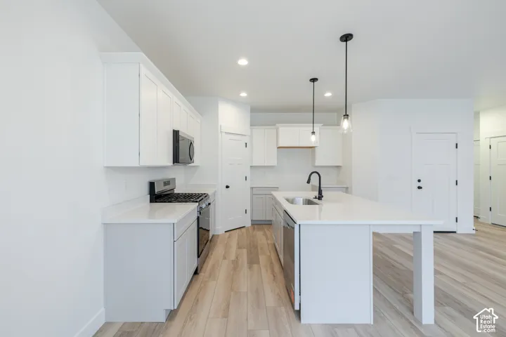 Kitchen featuring white shaker-style cabinetry, quartz countertops, a central island with a matte black faucet, and wood-finish flooring