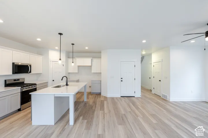 Kitchen featuring white shaker-style cabinetry, quartz countertops, a central island with a matte black faucet, stainless steel appliances, and wood-finish flooring