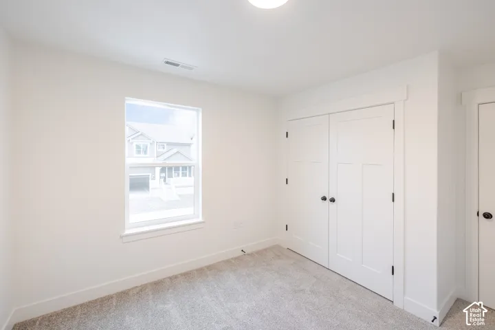 Neutral carpeted flooring, single-pane window with white casing, and dual-panel closet doors featuring matte black hardware