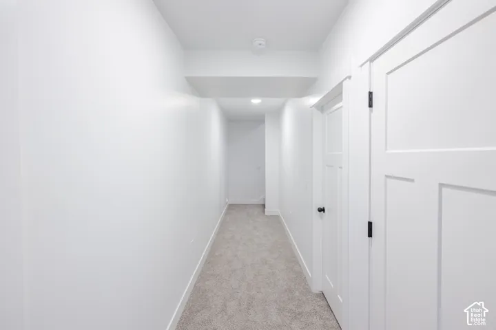 Hallway featuring neutral-toned carpeting, crisp white walls, and interior doors with matte black hardware