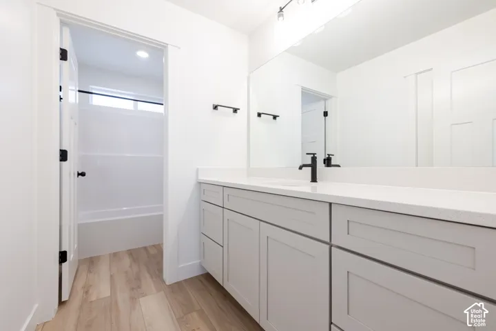 Bathroom featuring a dual-drawer vanity with a stone-composite countertop, matte black faucet, wall-to-wall mirror, and wood-finish flooring