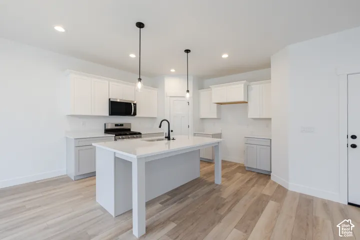 Kitchen featuring white shaker-style cabinetry, a central island with a quartz countertop, wood-finish flooring, two modern pendant lights, and a matte black faucet