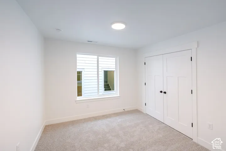 Neutral interior space featuring crisp white walls, carpeted flooring, a flush-mount overhead light fixture, dual-panel closet doors with matte black hardware, and a single-hung window with a flat casing