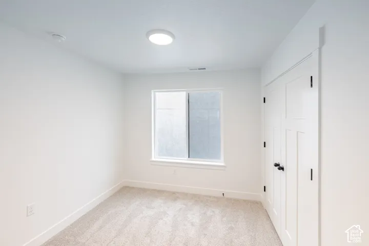Neutral-toned carpeted flooring, white walls, dual-door closet with matte black hardware, and a single-pane sliding window