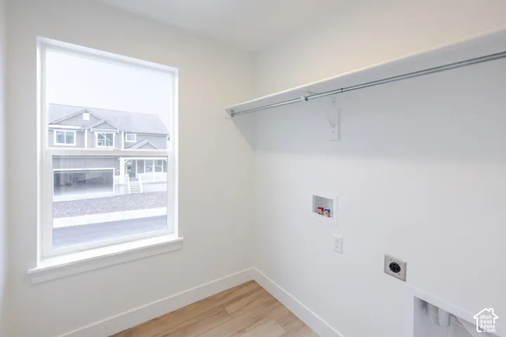 Utility area featuring wood-finish flooring, a single-hung window, built-in shelving with a metal garment rod, and dedicated appliance hookups