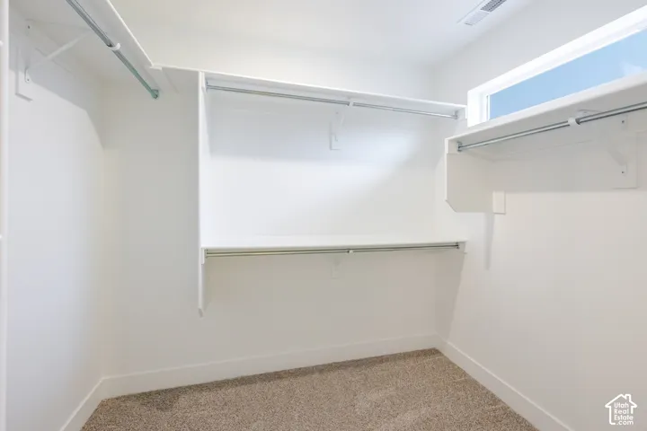 Walk-in closet featuring tiered white built-in shelving, metal hanging rods, wall-to-wall carpeting, and an elevated horizontal window