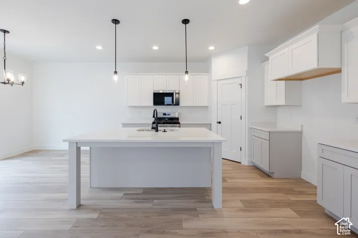 Kitchen featuring white shaker-style cabinetry, quartz countertops, a central island with a double-basin sink, pendant lighting, and wood-finish flooring
