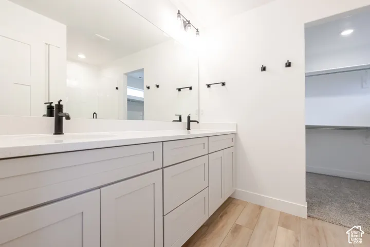Double vanity featuring light-colored shaker cabinetry, stone-style countertops, matte black plumbing fixtures, and a wall-to-wall mirror