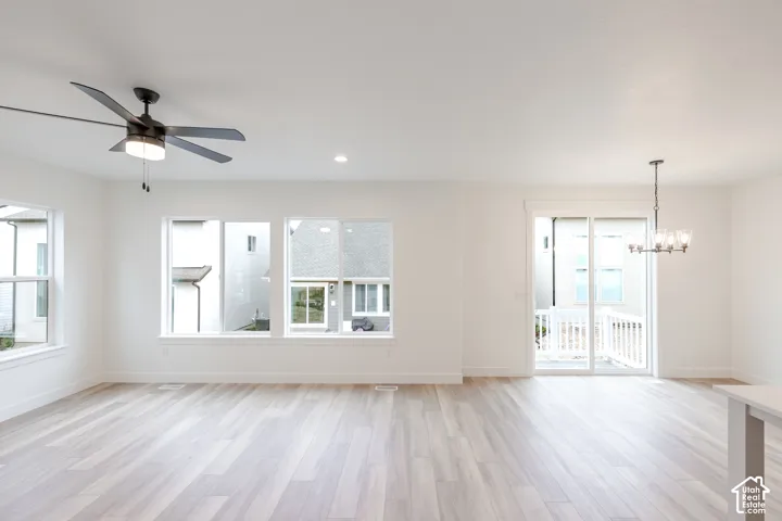 Open-concept space featuring light-toned wood-finish flooring, recessed lighting, a modern ceiling fan with integrated light, a tiered chandelier, and sliding glass doors
