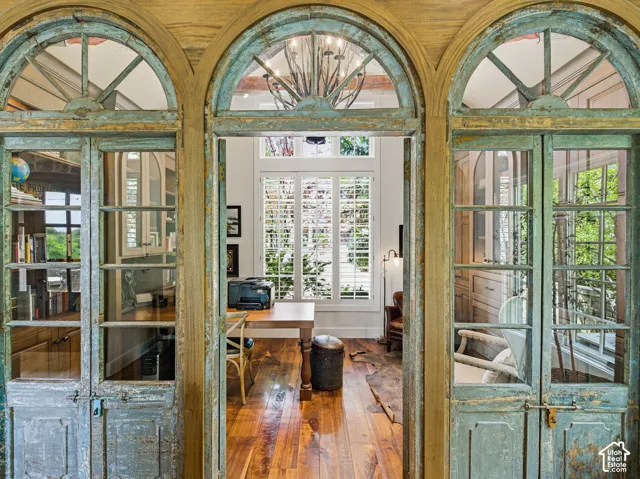 Arched entryways with distressed wood-finish doors open to a room featuring wide plank wood-finish flooring, white plantation shutters, a vaulted ceiling, and built-in cabinetry