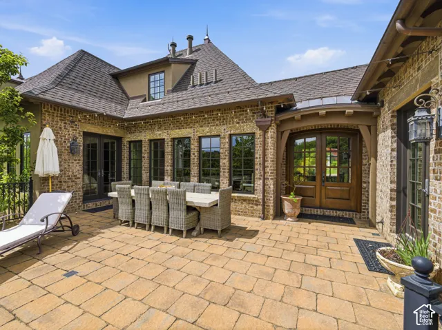 Expansive paver patio with a brick exterior, multiple windows, and a prominent double entry door with glass panels